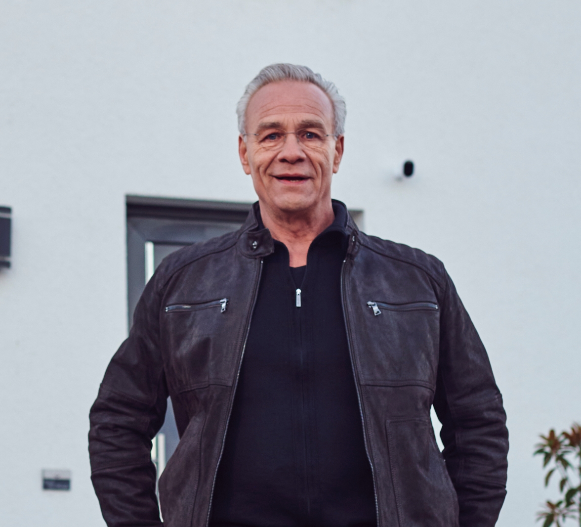 Klaus J. Behrendt, Schauspieler und TV-Kommissar, steht vor einem Haus mit einer Arlo Sicherheitskamera im Hintergrund