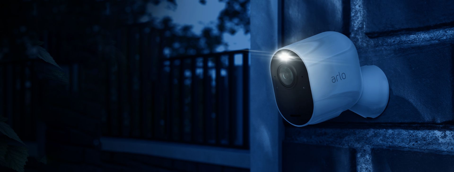 La caméra de surveillance Arlo Ultra accrochée contre un mur qui filme dans la nuit avec son projecteur intégré.