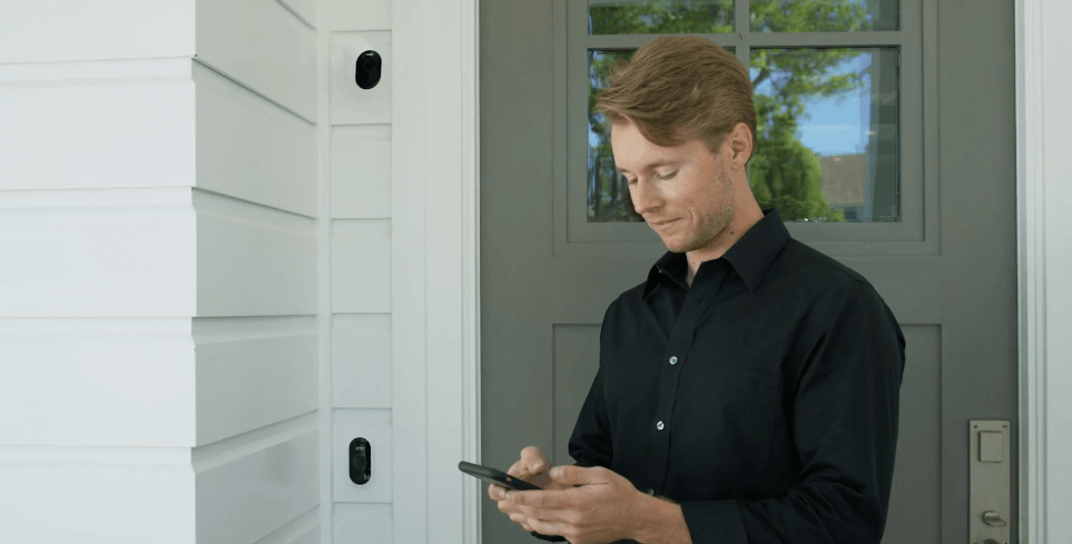 A man stands outside a door looking down at his mobile phone screen smiling