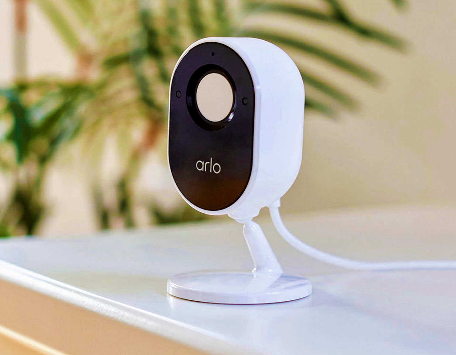 An Arlo Essential Indoor security camera placed on a shelf, captures live action and has a privacy shield which can be closed when set to disarm mode