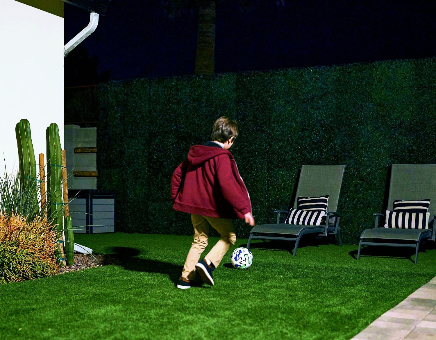 En ung pojke spelar fotboll i trädgården på natten