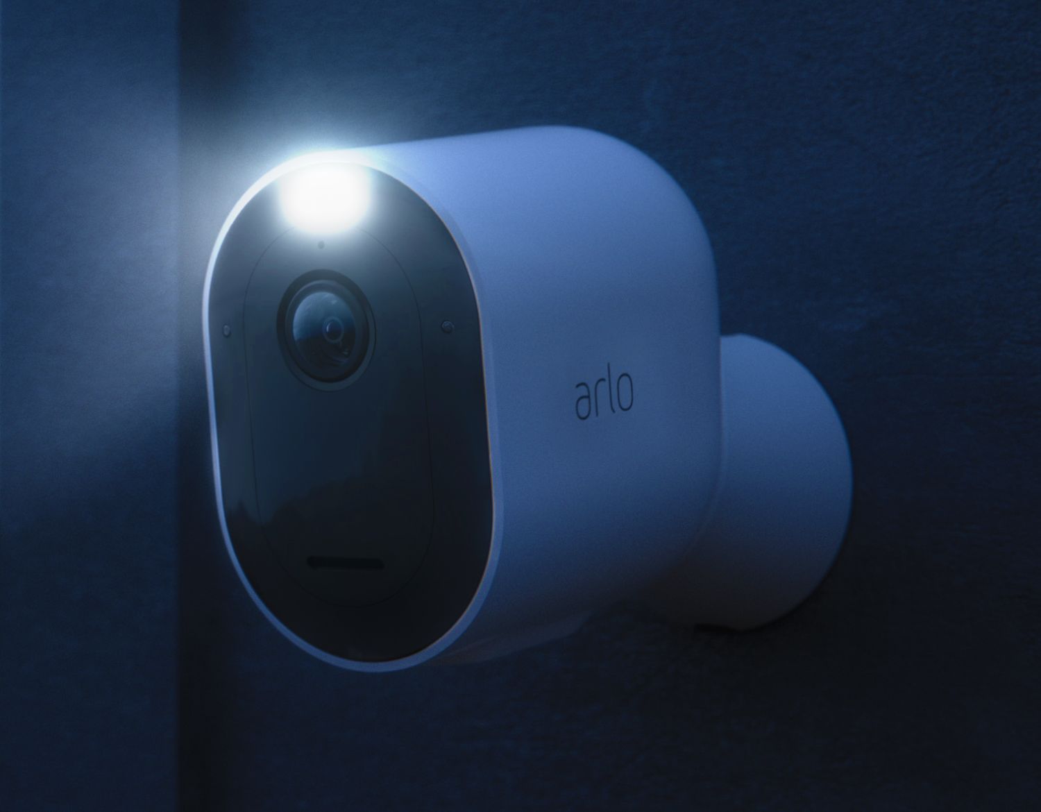 A close up view of an Arlo  camera on a wall outside at night with spotlight activated