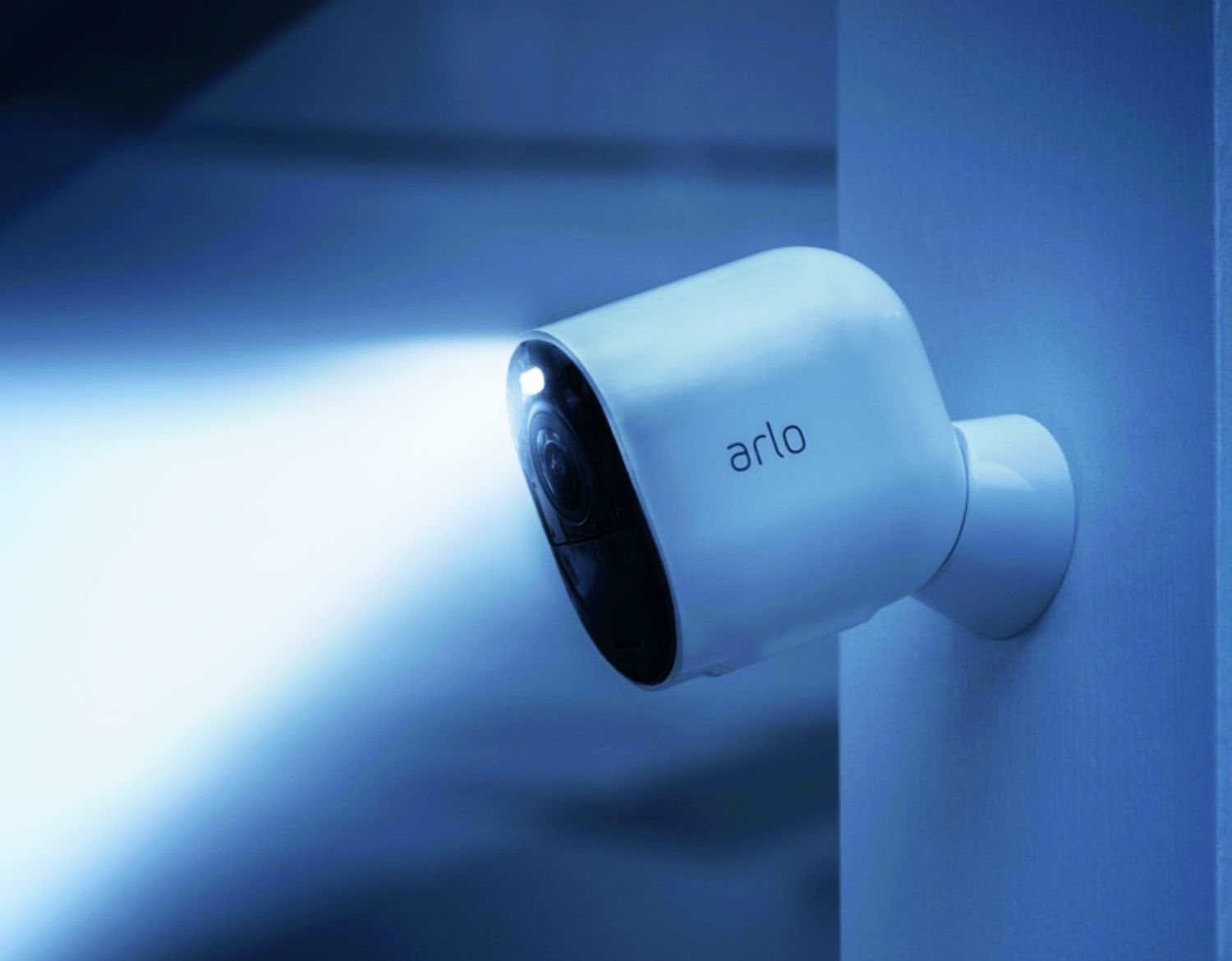 A white Arlo Ultra 2 security camera shines from a wall with a bright  spotlight 