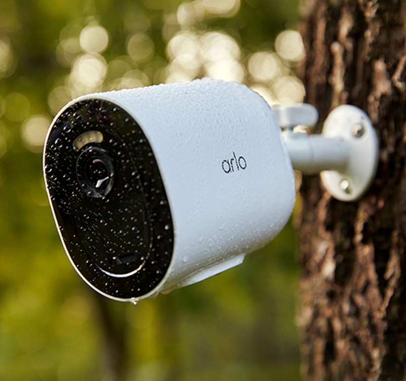 Una telecamera di sicurezza Arlo Go 2 che si appende a un albero sotto la pioggia ed è resistente all'acqua grazie al suo design resistente alle intemperie.