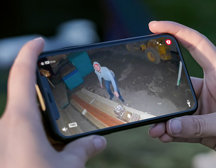 En hånd som holder en mobiltelefonskjerm viser noen som lurer i en bakhage om natten