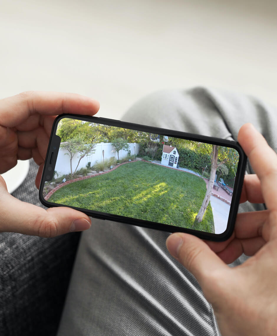 La vidéo de surveillance d’une caméra de sécurité Arlo sur le smartphone en live avec la vision à 180 degrés montre le jardin d’une maison.