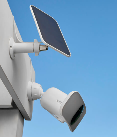 Die Arlo Pro 3 Flutlicht-Überwachungskamera, die an der Wand hängt und durch das Arlo Solarpanel aufgeladen wird