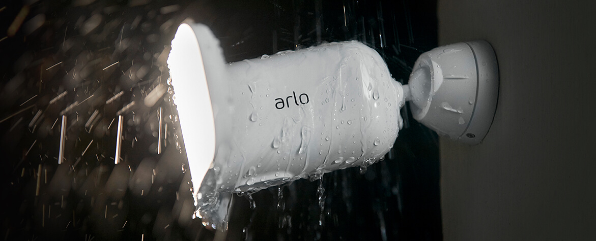 An Arlo Pro 3 Floodlight security camera up close hanging against a wall in the rain at night