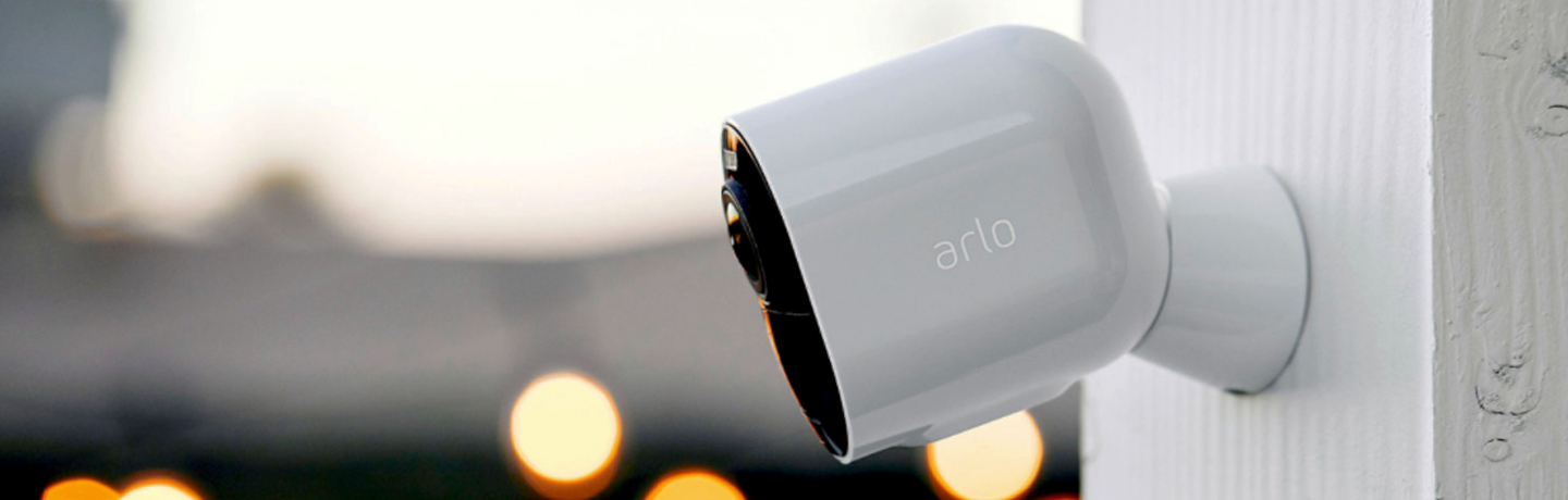 Arlo Ultra 2 Security Camera, mounted outside on white pillar, with bokeh lights in background