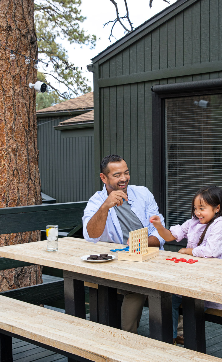 Father and daughter playing connect 4 on a picnic table, outside the cabin